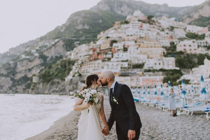 Couple during their elopement kissing with the hills of Positano in the background